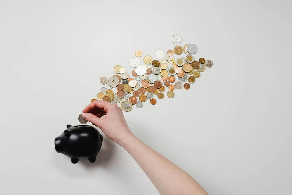 Mano echando monedas a una alcancía en forma de cochito