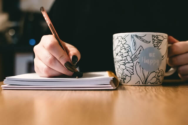 Persona escribiendo un libro sosteniendo una tasa.