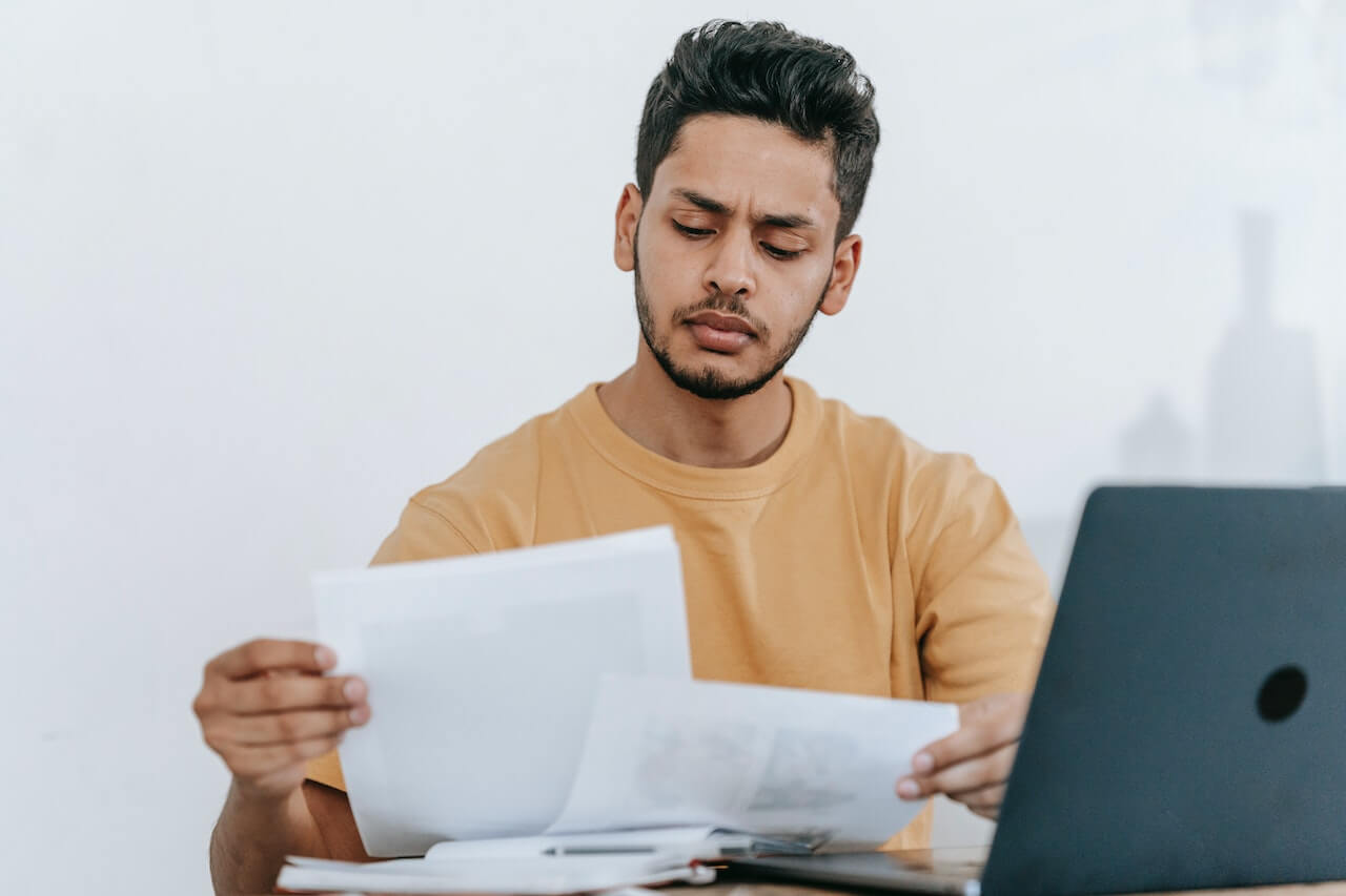 Persona leyendo documentos frente a una computadora